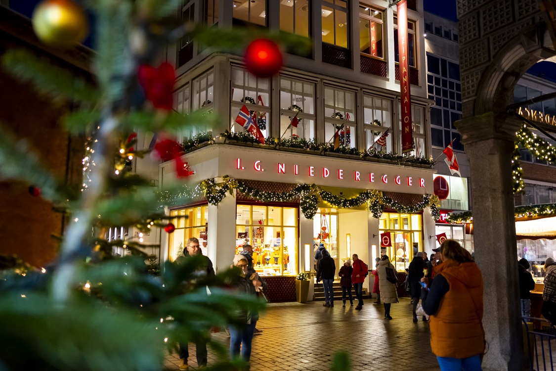 Stammhaus von Niederegger in der Breiten Straße zur Weihnachtszeit, festlich dekoriert und beleuchtet, im Vordergrund Menschen auf der Straße.